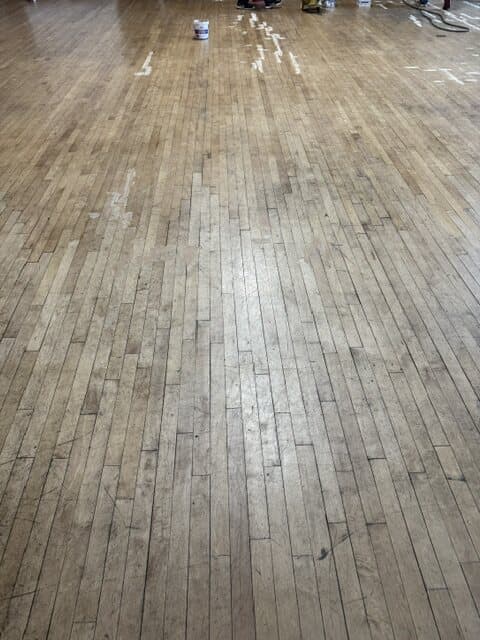 The hall floor before the work: a wide maple strip floor, scuffed and paint-marked from years of use