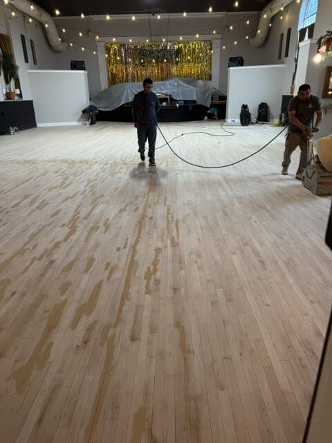 The same floor sanded back to raw pale wood, with two of the crew running the sander