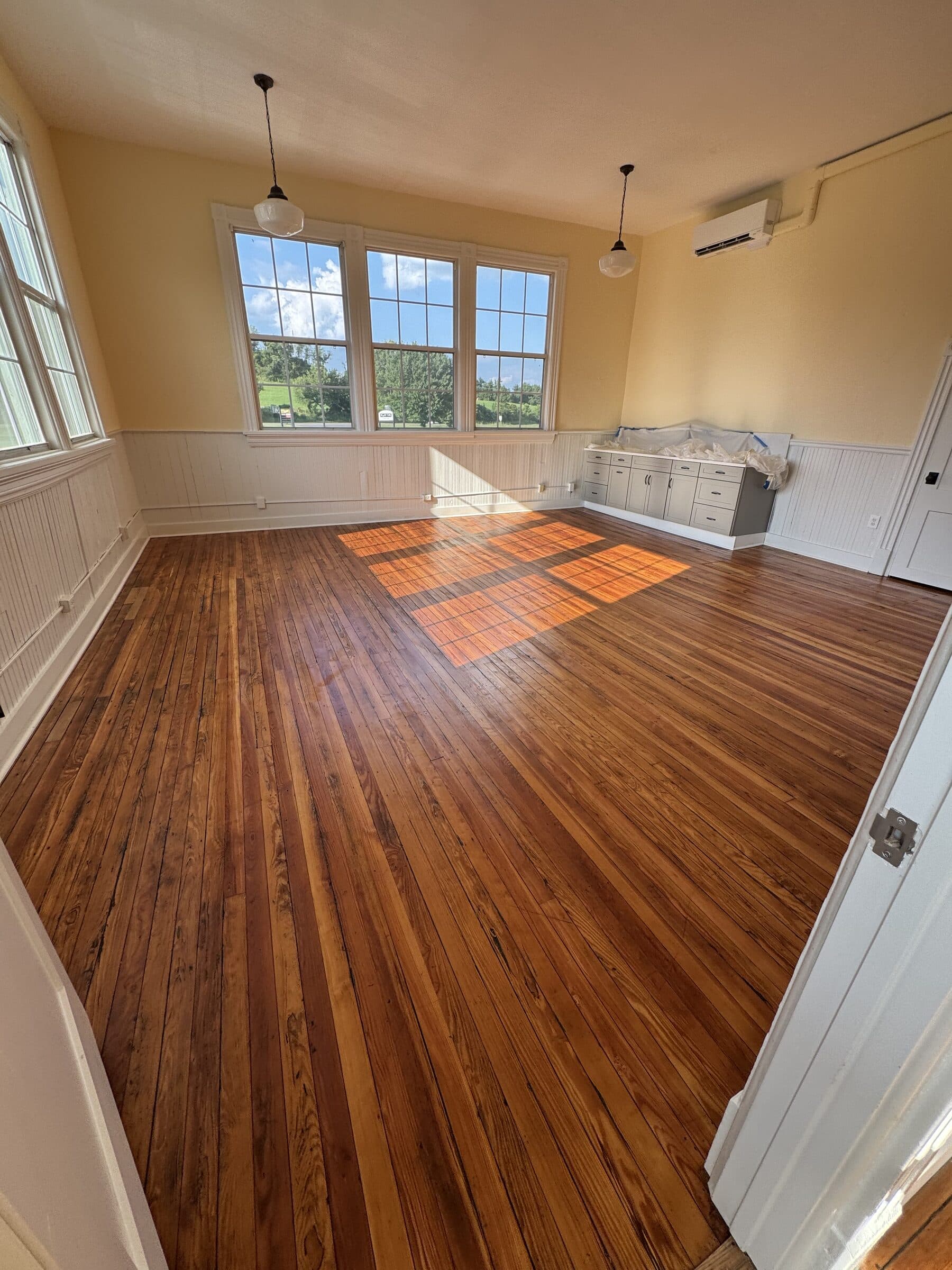 The refinished hundred-year-old classroom floor at the Sperryville School House, under tall windows and schoolhouse pendant lights