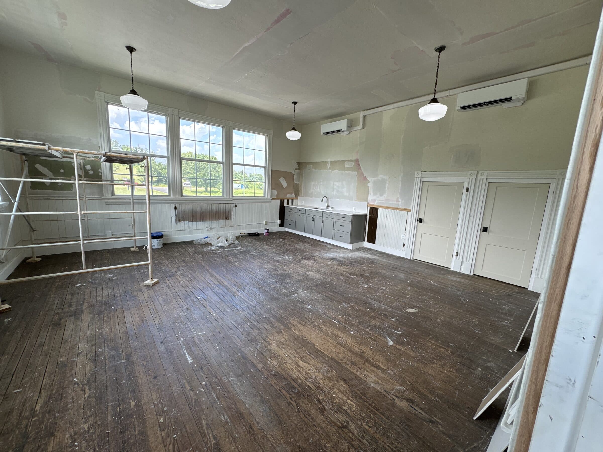 The classroom before the work: bare, paint-spattered floorboards, scaffolding against the wall, new cabinets already fitted