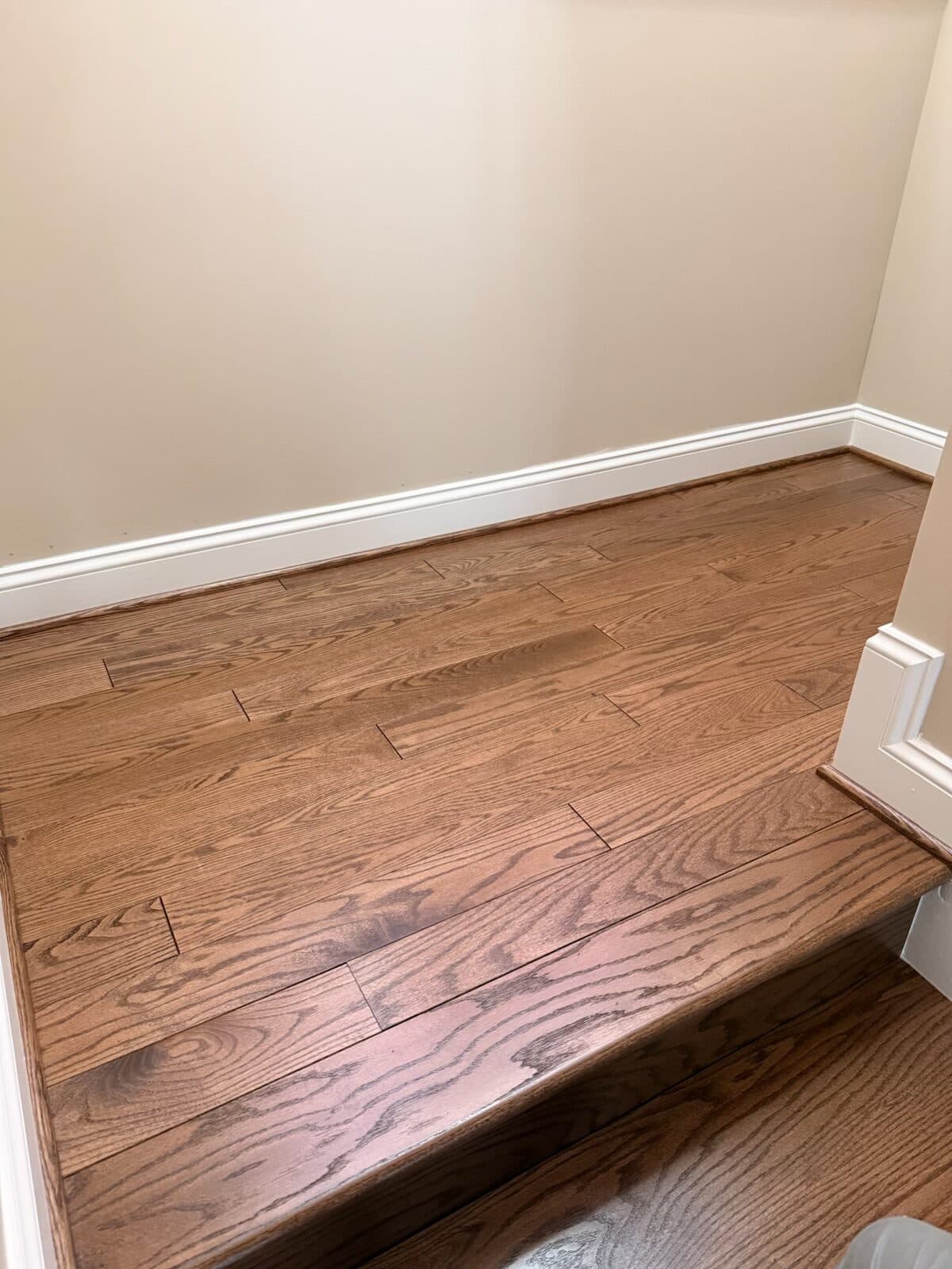 After: the same landing laid in hardwood, meeting the white baseboard